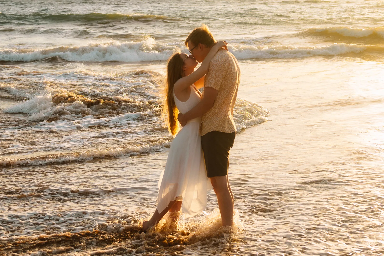 A couple holding each other as warm evening light rakes across the shorebreak