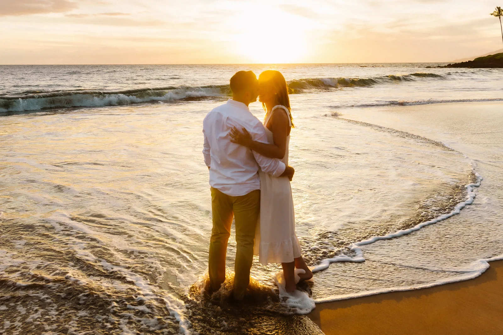 A couple silhouetted against the sun as it drops into the water behind them