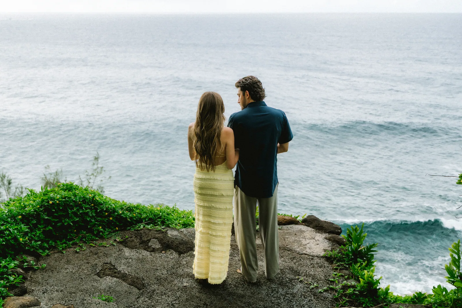 A couple standing at a cliff overlook watching the water below
